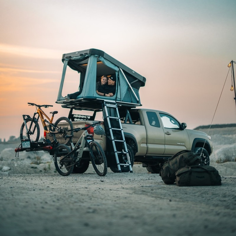 Thule Widesky roof top tent hard shell on car roof with people inside and bike carrier